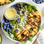 Creamy citrus dressing seared pineapple salad with charred pineapple rings, blueberries, blackberries, avocado, greens, and creamy citrus dressing in a bowl.