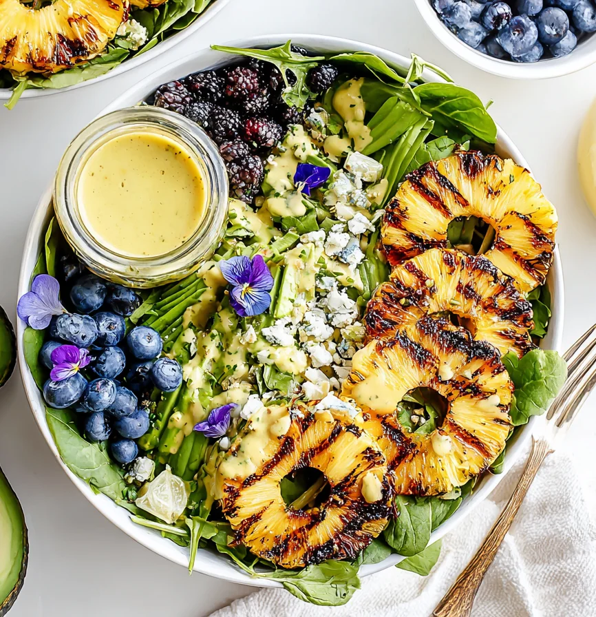 Creamy citrus dressing seared pineapple salad with charred pineapple rings, blueberries, blackberries, avocado, greens, and creamy citrus dressing in a bowl.