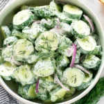 Overhead bowl of Cucumber Dill Salad with creamy yogurt dressing, sliced cucumbers, fresh dill, and red onion, served with herbed bread.