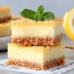 Creamy Lemon Squares stacked with buttery graham cracker crust and silky lemon filling, topped with fresh mint and served beside a lemon.
