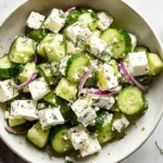 Cucumber Feta Salad with Lemon Greek Vinaigrette topped with dill, red onion, and feta cubes, served with a small bowl of lemon-olive oil dressing.