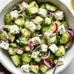 Cucumber Feta Salad with Lemon Greek Vinaigrette in a bowl with diced cucumbers, feta cubes, red onion, and fresh herbs.