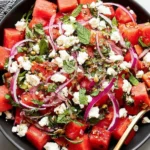 Feta Watermelon Salad with juicy watermelon cubes, crumbled feta, fresh mint, and red onion tossed in a honey-balsamic dressing in a black bowl.