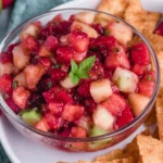 Fruit Salsa with Cinnamon Sugar Tortilla Chips in a glass bowl with diced strawberries, apples, kiwi, and raspberries, garnished with mint and served with cinnamon sugar chips.