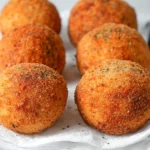 Freshly fried Arancini Italian Rice Balls cooling on a rack, golden and crunchy with a light sprinkle of herbs.