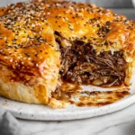 Steak and Onion Meat pie with flaky golden puff pastry, sliced open to show rich beef and onion gravy filling.