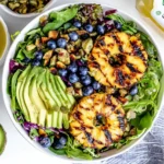 Creamy citrus dressing seared pineapple salad with grilled pineapple rings, sliced avocado, blueberries, pepitas, and mixed greens in a white bowl.