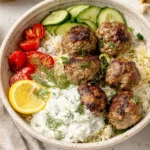 Gyro Bowls with browned meatballs, creamy tzatziki, fluffy lemon rice, sliced cucumbers, cherry tomatoes, fresh dill, and a lemon wedge in a bowl.