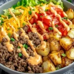 High Protein Burger Bowls topped with seasoned ground beef, shredded cheddar, diced tomatoes, crunchy lettuce, roasted potatoes, and creamy burger sauce.