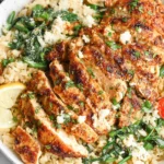 Lemon Garlic Parmesan Chicken & Rice bowl topped with sliced golden chicken, spinach, cherry tomatoes, feta, and fresh lemon wedges.