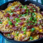 Irish Pub Potato Nachos in a cast-iron skillet topped with melted cheddar jack, crispy bacon, and chopped green onions on a rustic blue table.