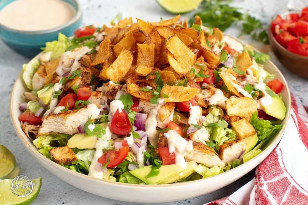 Santa Fe Chicken Salad piled high with taco-seasoned chicken, romaine, cherry tomatoes, red onion, avocado, cilantro, creamy dressing, and crunchy tortilla strips.