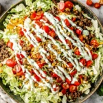 Taco Salad in a large bowl with seasoned ground beef, romaine, cherry tomatoes, corn, shredded cheese, and creamy cilantro-lime dressing drizzle.