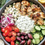 Low-Carb Greek Chicken Bowls with grilled chicken, cucumber, tomatoes, feta, olives, and creamy tzatziki sauce in a meal prep bowl.
