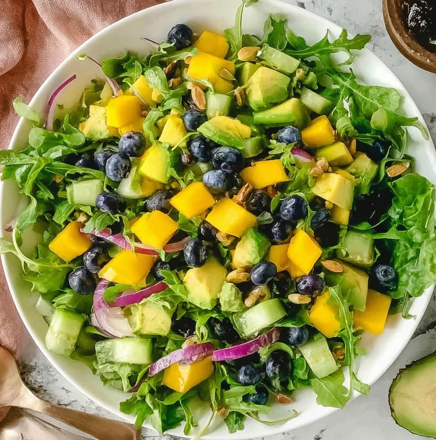 Mango Cucumber Salad with blueberries, avocado, arugula, red onion, and pepitas, drizzled with cilantro lime vinaigrette.