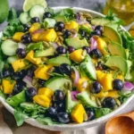 Mango Cucumber Salad with blueberries, avocado, arugula, and toasted walnuts in a bowl with cilantro lime vinaigrette.