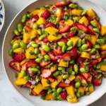 Overhead view of Mango Strawberry Avocado Edamame Salsa with mango, strawberries, edamame, herbs, and red onion, served with tortilla chips.