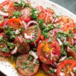 Marinated Tomatoes Salad on an oval platter with sliced tomatoes, red onion, fresh herbs, and olive oil vinegar marinade.