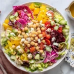 Mediterranean Chopped Salad served in a bowl with chickpeas, feta, cucumber, tomatoes, peppers, and radicchio, with oregano vinaigrette on the side.