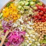 Mediterranean Chopped Salad in a wooden bowl with chickpeas, feta, cucumbers, cherry tomatoes, peppers, and oregano vinaigrette.