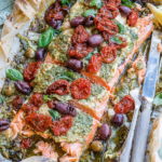 Mediterranean Salmon in Parchment Paper topped with pesto, sun-dried tomatoes, kalamata olives, capers, and fresh herbs, baked until flaky and juicy.