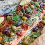 Mediterranean Salmon in Parchment Paper baked with pesto, kalamata and green olives, sun-dried tomatoes, fresh dill, and lemon wedges for a juicy, flavorful dinner.