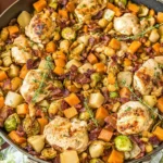 One-Pot Easy Harvest Chicken Skillet in a large pan with juicy chicken, crispy bacon, sweet potatoes, Brussels sprouts, apples, cranberries, and thyme.