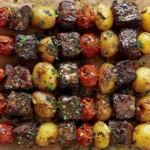 Rosemary Garlic Steak Kebabs on skewers with grilled sirloin cubes, baby potatoes, and blistered grape tomatoes, finished with rosemary and garlic drizzle.