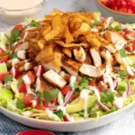 Santa Fe Chicken Salad in a bowl with sliced taco-seasoned chicken, romaine, tomatoes, red onion, avocado, cilantro, creamy dressing, and crunchy tortilla strips.