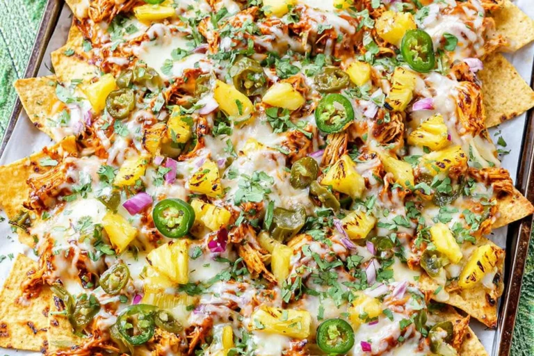 BBQ Chicken and Grilled Pineapple Nachos on a sheet pan with melted cheese, charred pineapple, jalapeños, red onion, and cilantro.