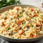 Simple Ground Turkey Pot Pie Pasta in a bowl with farfalle, carrots, peas, and creamy sauce, garnished with herbs.
