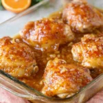 Baked Apricot Chicken Thighs in a glass baking dish, coated in a glossy sweet-and-savory apricot glaze with bits of onion and garlic.
