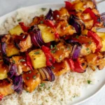 Baked Pineapple Chicken Kabobs drizzled with sticky pineapple glaze, skewered with red pepper and red onion, served over white rice.