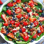 Strawberry Spinach Salad with fresh spinach, sliced strawberries, blueberries, toasted pecans, feta, and balsamic glaze in a white bowl.