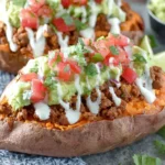 Taco Stuffed Sweet Potatoes topped with seasoned taco beef, creamy guacamole, pico de gallo, and a sour cream drizzle.