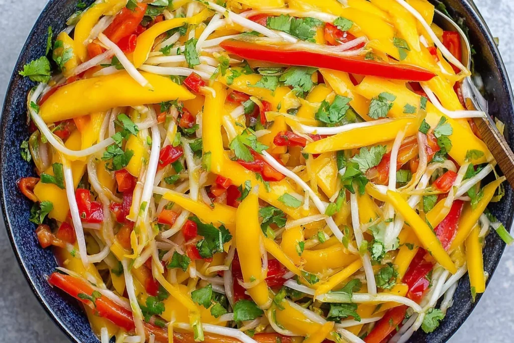 Thai Mango Salad in a blue bowl with mango strips, bean sprouts, red bell pepper, cilantro, and lime-chili dressing.