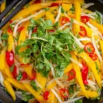 Thai Mango Salad in a black bowl with sliced mango, bean sprouts, red chili, and fresh cilantro.