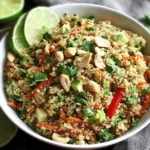 Thai Quinoa Crunch Salad in a white bowl with lime wedges, cilantro, and crunchy peanuts.