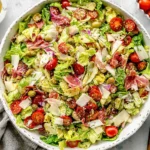 Italian Chopped Salad in a large bowl with romaine, cherry tomatoes, olives, pepperoncini, artichoke hearts, mozzarella, and shaved parmesan.