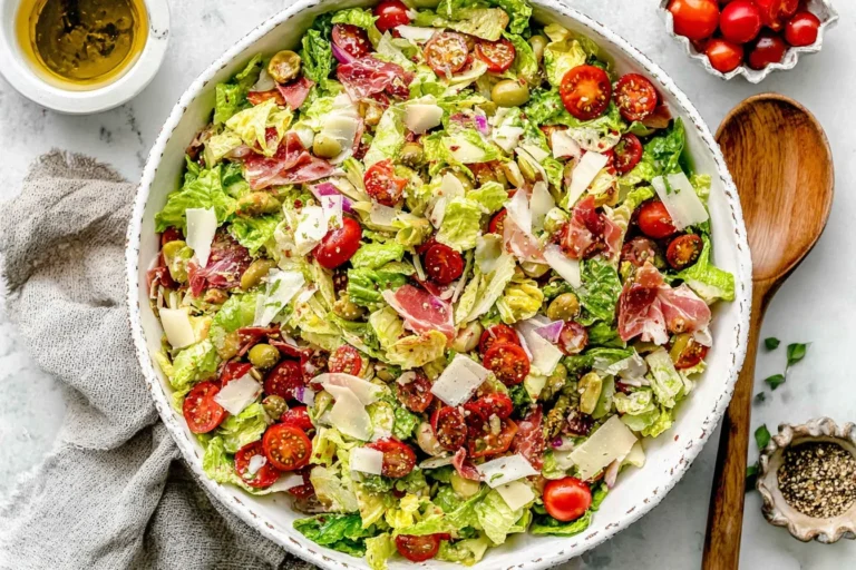 Italian Chopped Salad in a large bowl with romaine, cherry tomatoes, olives, pepperoncini, artichoke hearts, mozzarella, and shaved parmesan.