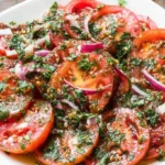 Marinated Tomatoes Salad with fresh herbs, red onion, and zesty vinaigrette on a white plate