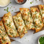 Chicken Alfredo Garlic Bread sliced on a wooden board with melted mozzarella, creamy chicken, parsley, and red pepper flakes.
