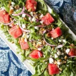 Watermelon Arugula Salad with feta, toasted walnuts, red onion, and mint on a white platter