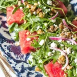 Watermelon Arugula Salad with feta, toasted walnuts, and red onion served on a blue-and-white plate
