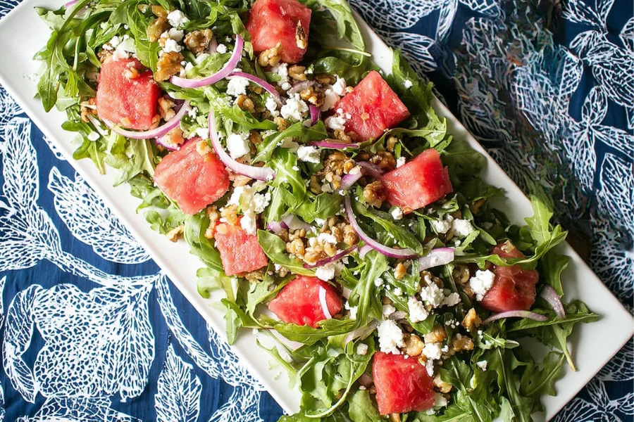 Watermelon Arugula Salad with feta, toasted walnuts, red onion, and mint on a white platter