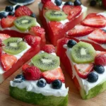Watermelon Pizza slices topped with creamy yogurt, strawberries, blueberries, raspberries, and kiwi on a wooden board