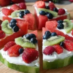 Watermelon Pizza slices with creamy yogurt, strawberries, blueberries, raspberries, and kiwi served on a wooden cutting board