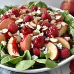 White Peach Raspberry Almond Salad with spring greens, sliced white peaches, fresh raspberries, feta, and crunchy almonds in a white bowl.