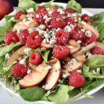 White Peach Raspberry Almond Salad piled high with spinach, sliced white peaches, fresh raspberries, crumbled feta, and almonds in a white bowl.