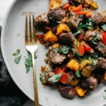 Whole30 steak bites with sweet potatoes and peppers on a gray plate, topped with fresh cilantro.